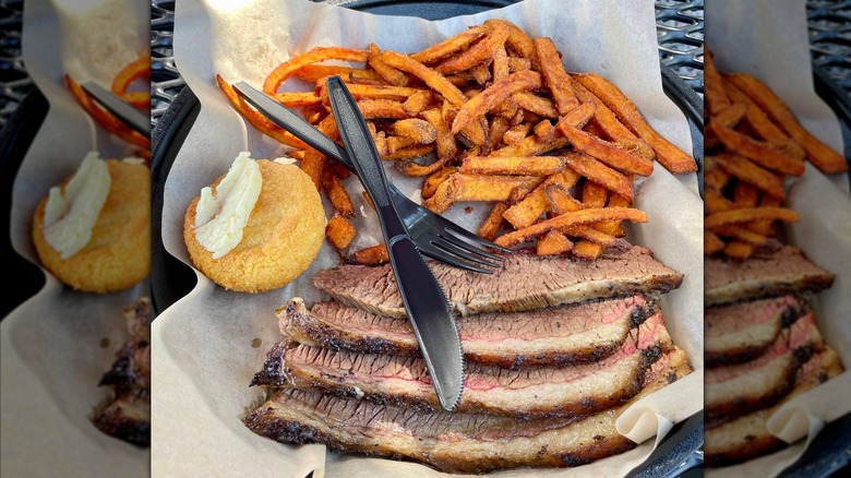 A cast iron tray with sliced brisket, served with sweet potato fries and a side of cornbread with butter