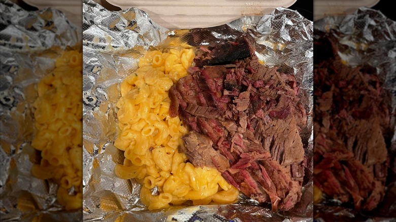 A foil-lined takeout container with chopped brisket and macaroni and cheese
