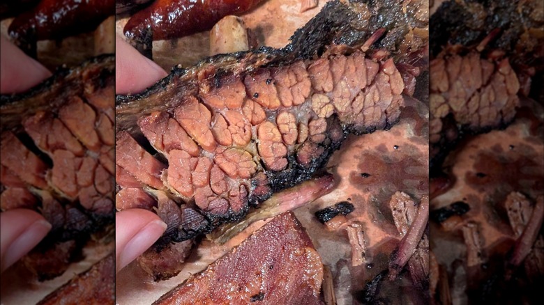 A close-up of smoked brisket with a dark bark and visible marbling being held over butcher paper with pieces of brisket