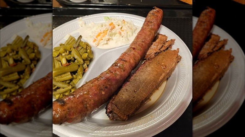 A barbecue plate with sliced brisket and a smoked sausage, served with coleslaw and green beans