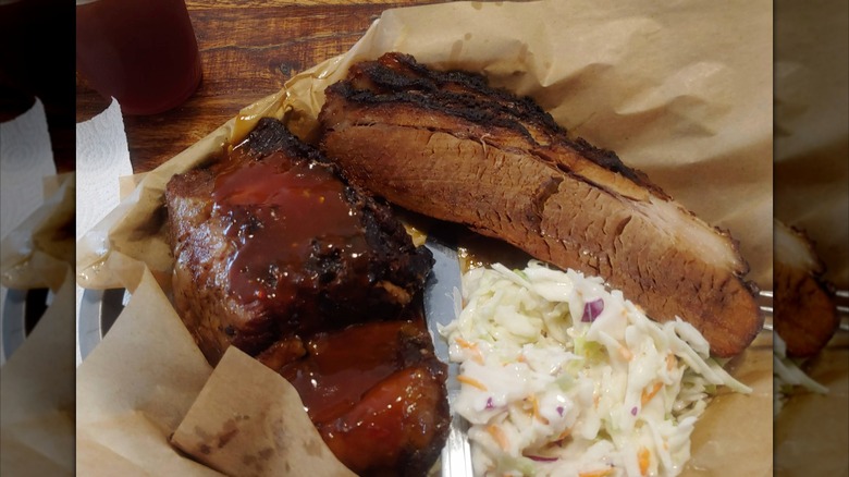A barbecue tray with sliced brisket and sauced ribs, served with a side of coleslaw