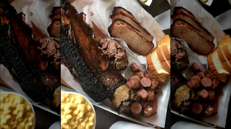 A barbecue tray with a beef rib, sliced brisket, and sausage, served with macaroni and cheese and sliced white bread