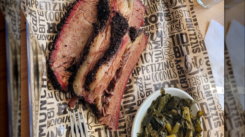A metal tray with sliced brisket, served with a side of braised greens