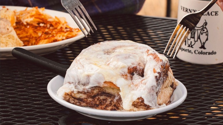 Two forks about to dig into a large frosted cinnamon roll