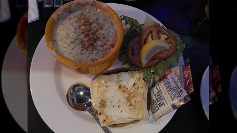 Open face grilled halibut sandwich with lettuce, tomato, lemon wedge, and side of salmon chowder