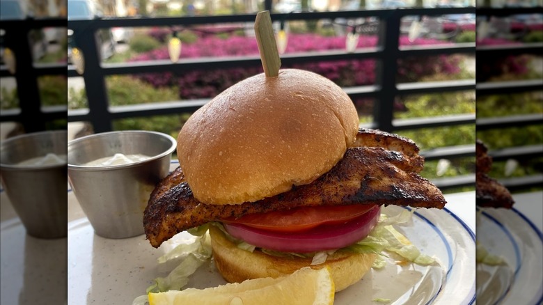 Blackened mahi mahi sandwich on bun with red onion, tomato, and lemon wedge on side