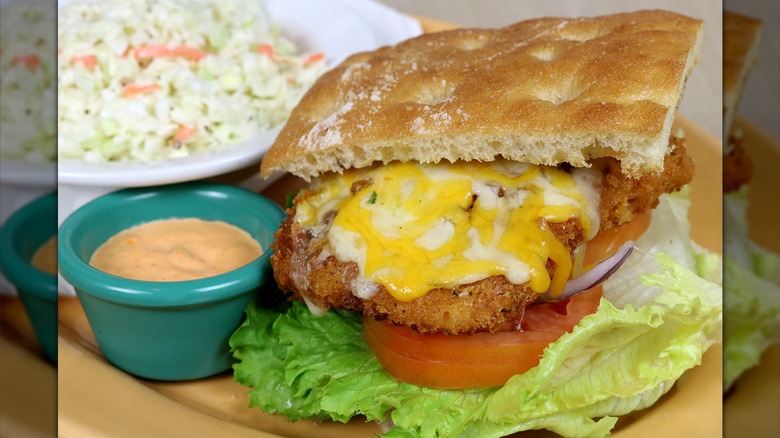 A panko cod sandwich with cheese, tomatoes, and lettuce on ciabatta bun