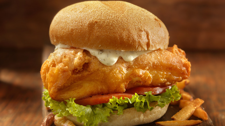 Close-up of a fish sandwich with tartar sauce, lettuce, and tomato