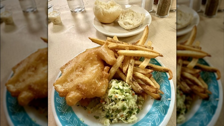 Plate of fish and chips next to plate with bun