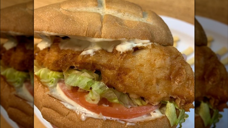 close up of fish sandwich with lettuce, tomato, and tartar sauce on bun