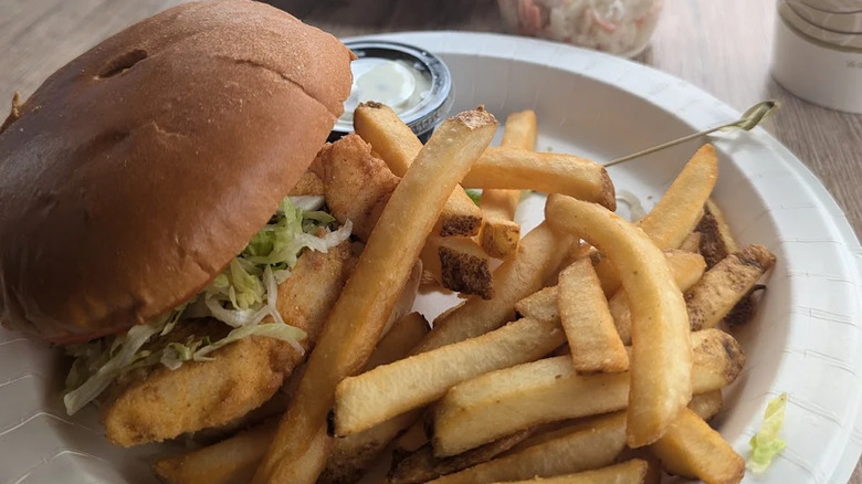 close up of fried haddock sandwich with fries and tartar sauce on paper plate
