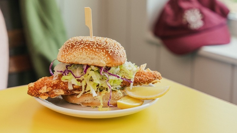 fish sandwich on sesame seed bun served with lemon wedge