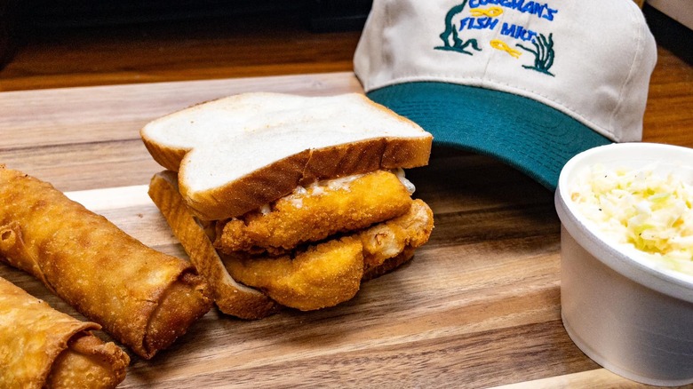 fish sandwich, egg rolls, side of coleslaw and Coleman's Fish Market ball cap on wooden surface