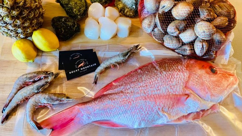 Whole fresh fish and shrimp on cutting board next to clams and rocky mountain seafood business card