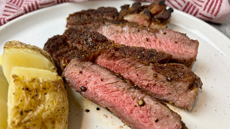 Cooked and sliced ribeye steak on plate with potatoes.
