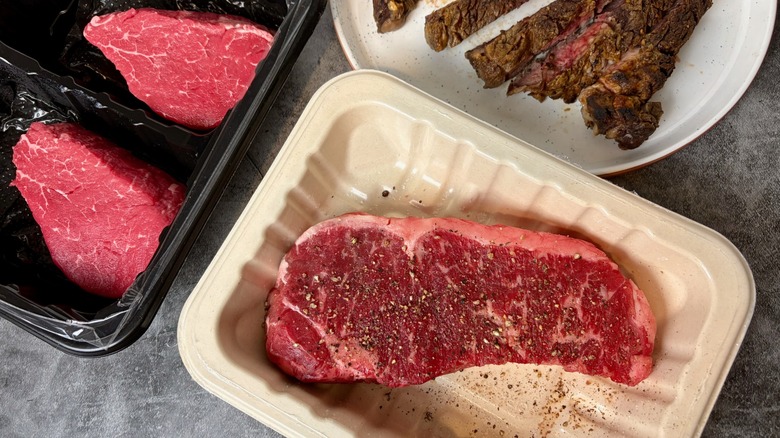 Different cuts of meat on counter, including seasoned ribeye and cooked steak.