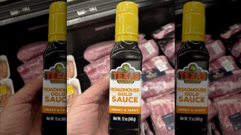 Hand holding a bottle of Texas Roadhouse gold sauce in a supermarket meat department