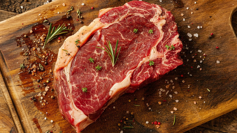 Raw ribeye steak on a cutting board with seasonings