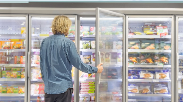 man shopping in frozen meal section of grocery store