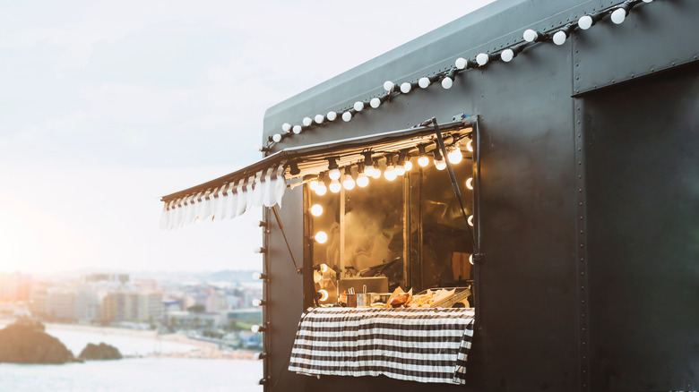 The open window of a food truck with lights on the awning
