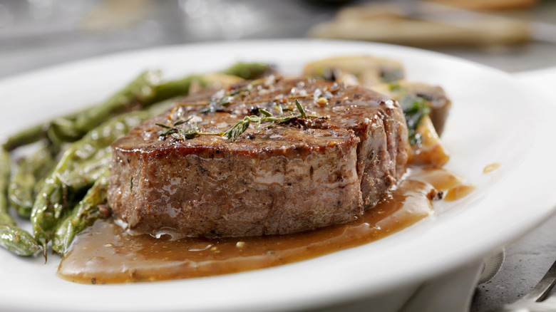 A steak on a plate with gravy and vegetables