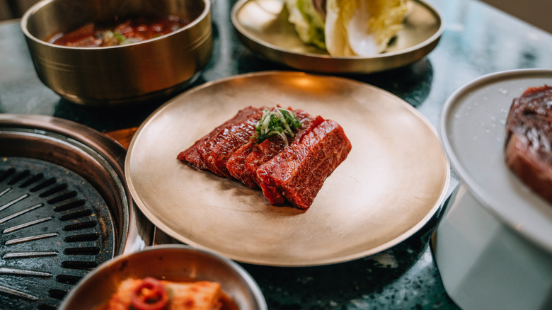 Fatty marbled steak on gold plate surrounded by other dishes