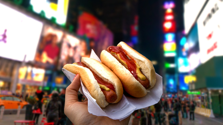 Hand holding two hot dogs with ketchup and mustard in Times Square