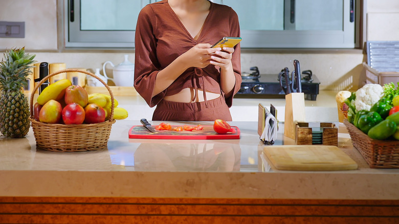 Young person in kitchen looking at smartphone and smiling