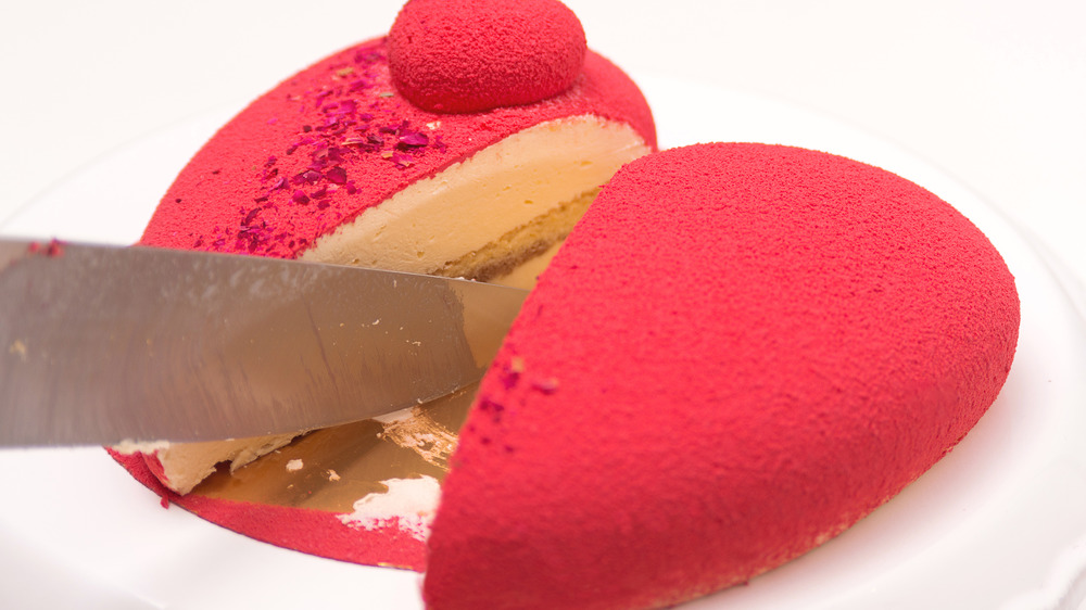 Knife cutting into red heart-shaped cake