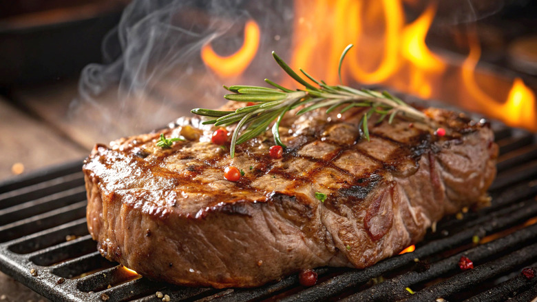Flame-grilled ribeye steak with herbs and peppercorns on BBQ grill