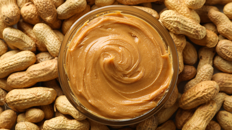 A bowl of creamy peanut butter surround by peanuts in the shell