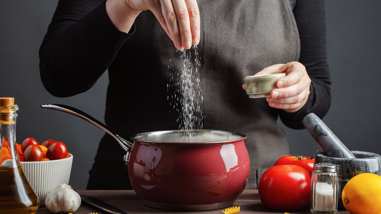 Person adding salt to a pot of pasta