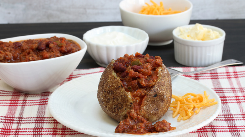 Baked potato with chili surrounded by toppings.