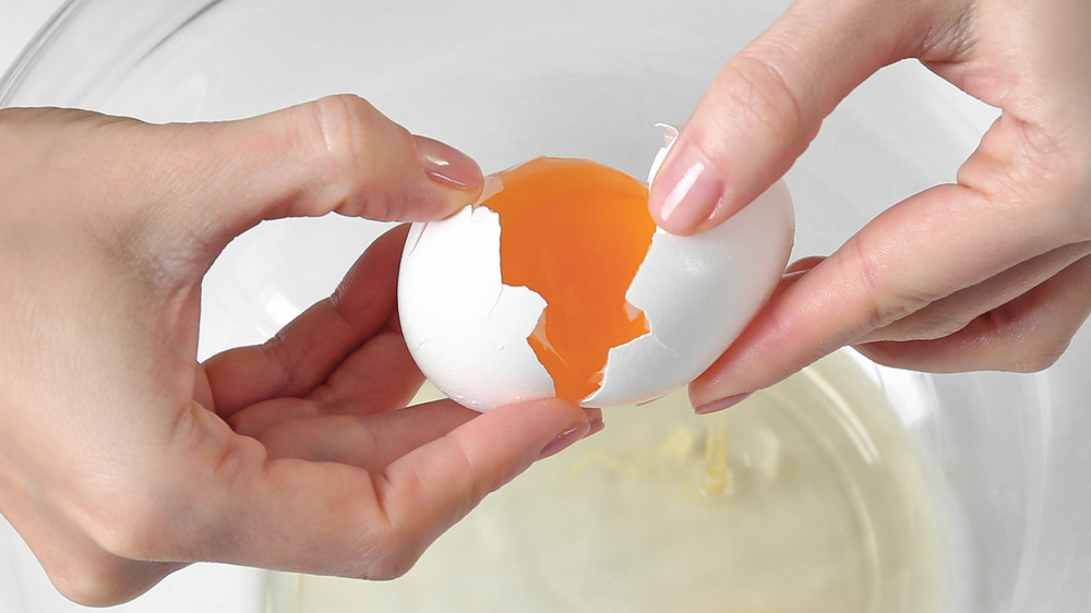 Hand holding two eggs cracking