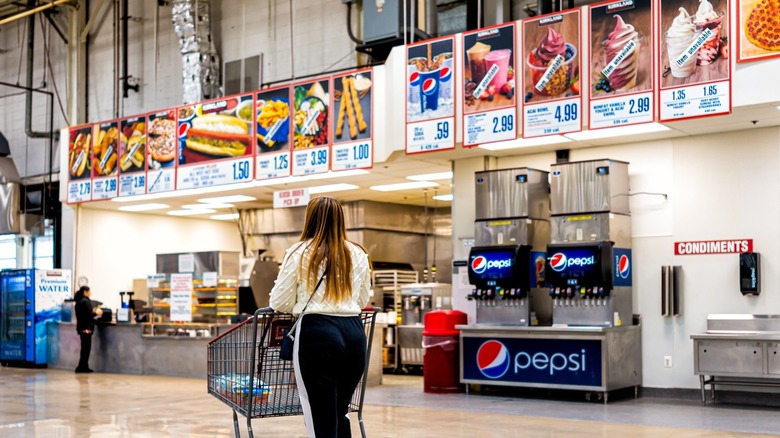 woman pushing cart in front of signs for Costco food court