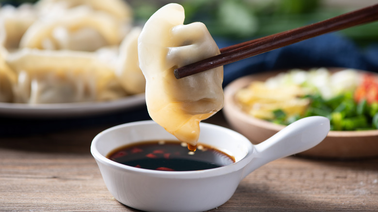 Chopsticks dipping dumpling into sauce on table with dishes of dumplings