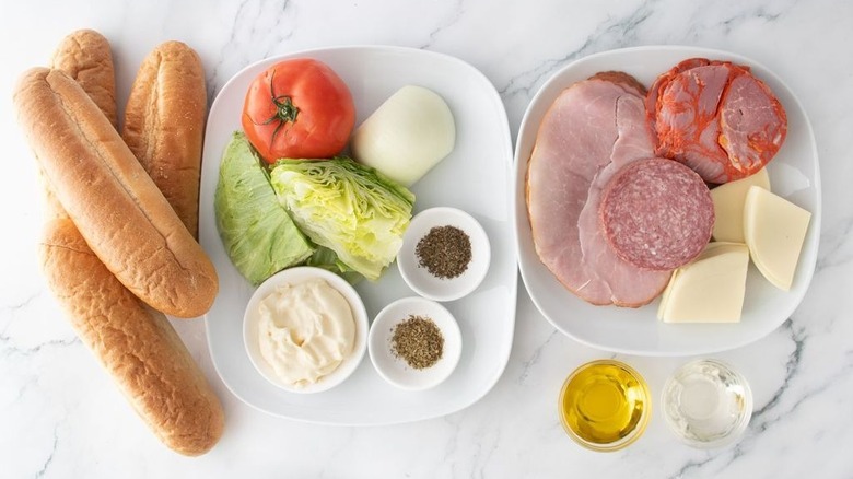 Hoagie rolls, tomato, cured meats, cheese, and other ingredients for copycat Jimmy John's Italian Night Club sandwiches laid out