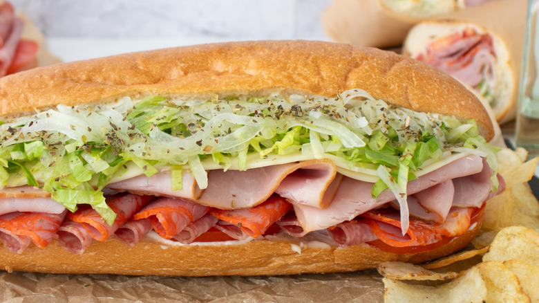 Close up of Italian Night Club sandwich on parchment paper with chips nearby
