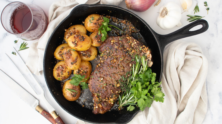 Steak and potatoes in skillet with herbs