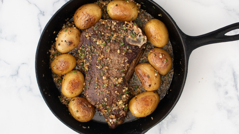 Steak and potatoes in skillet with melted compound butter