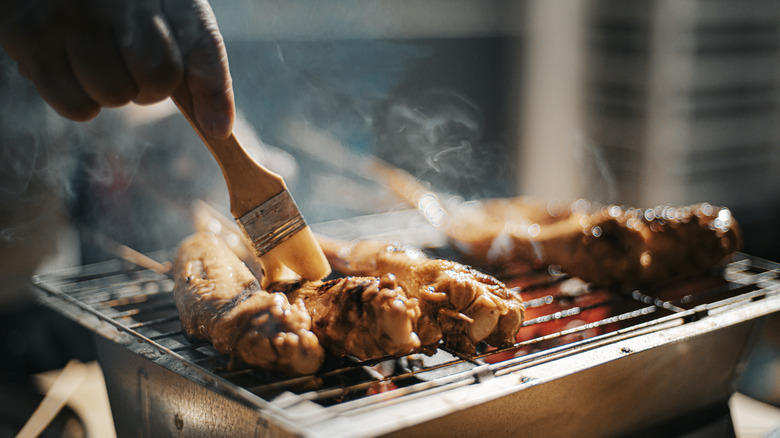 Hand brushing chicken skewers on grill
