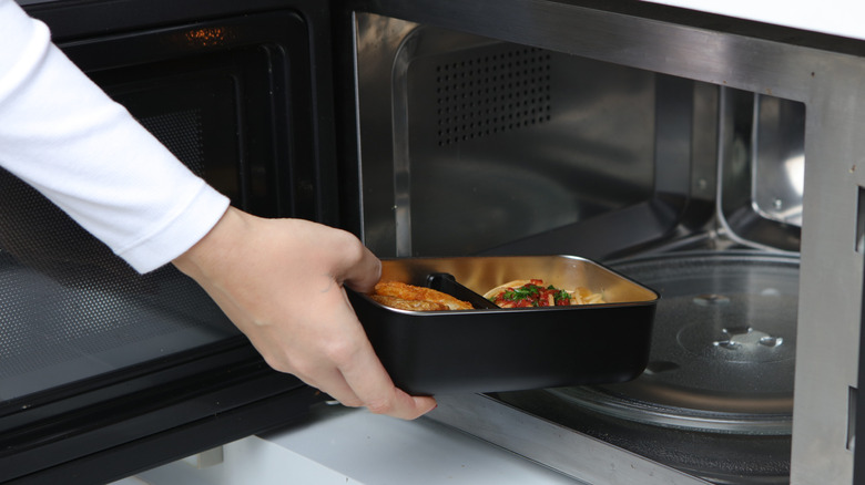 Person putting food container into microwave