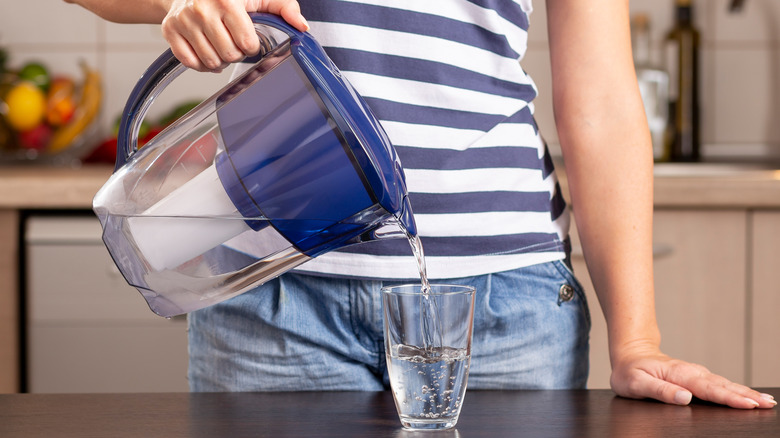 Woman pouring water from filtered pitcher into glass