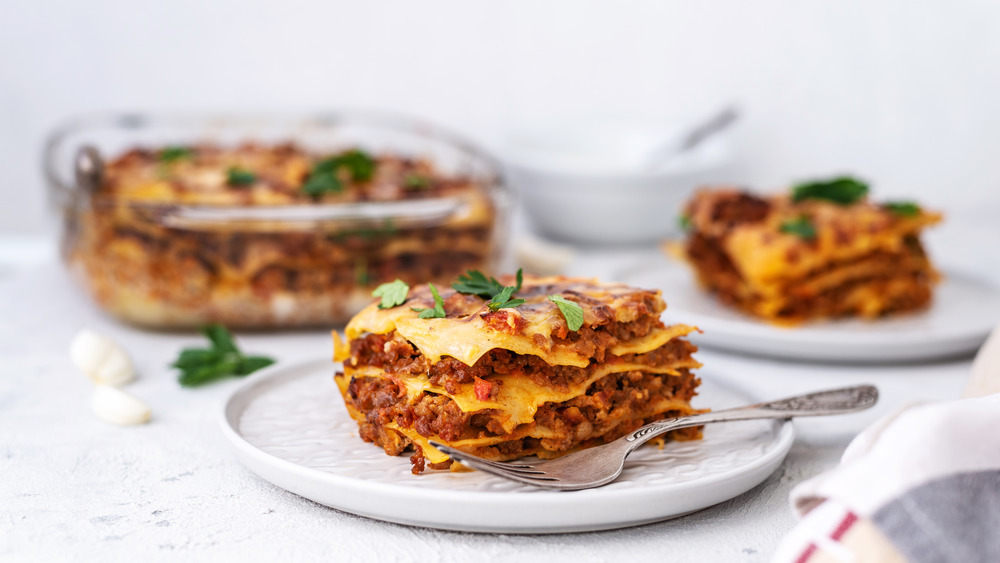 cooked lasagna with two plates of sliced lasagna