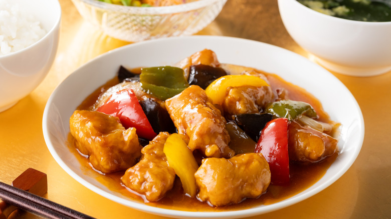 Sweet and sour pork with veggies in a white bowl