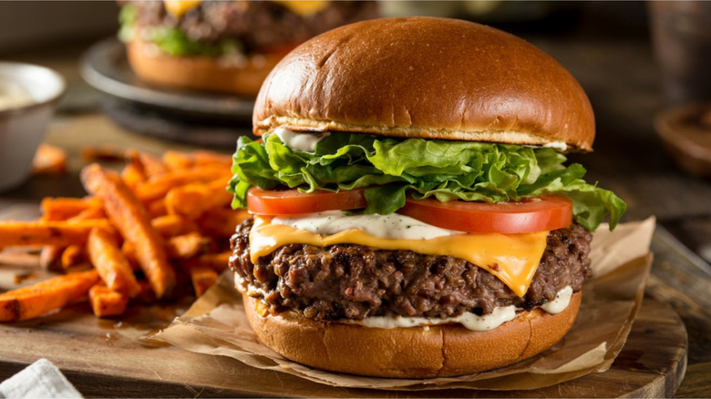 A gourmet burger with a side of fries on butcher paper on a wooden cutting board