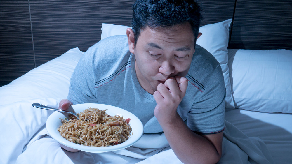 Man eating noodles in bed