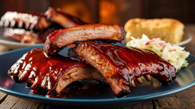 Pork ribs on a plate with coleslaw and cornbread in the background
