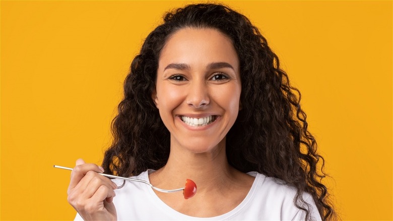 Smiling woman holding fork with tomato on it