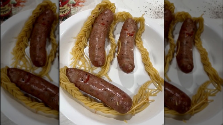 Sausage with braided noodles sticking out of the top on paper plate
